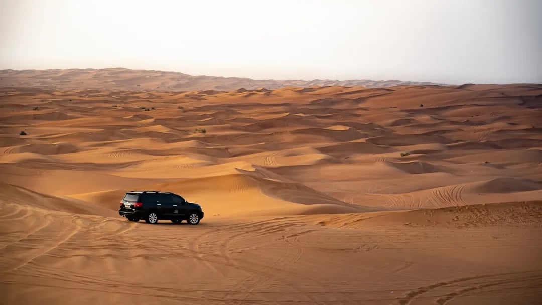Toyota Land Cruiser driving through Dubai desert dunes in golden hour light